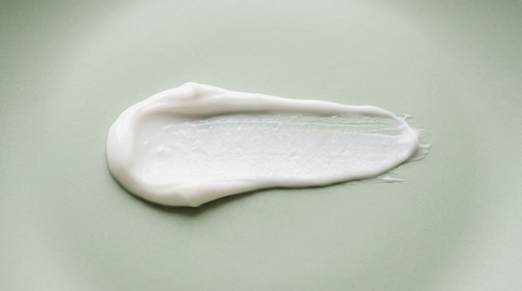 Smooth white cream swatch on a muted green surface,